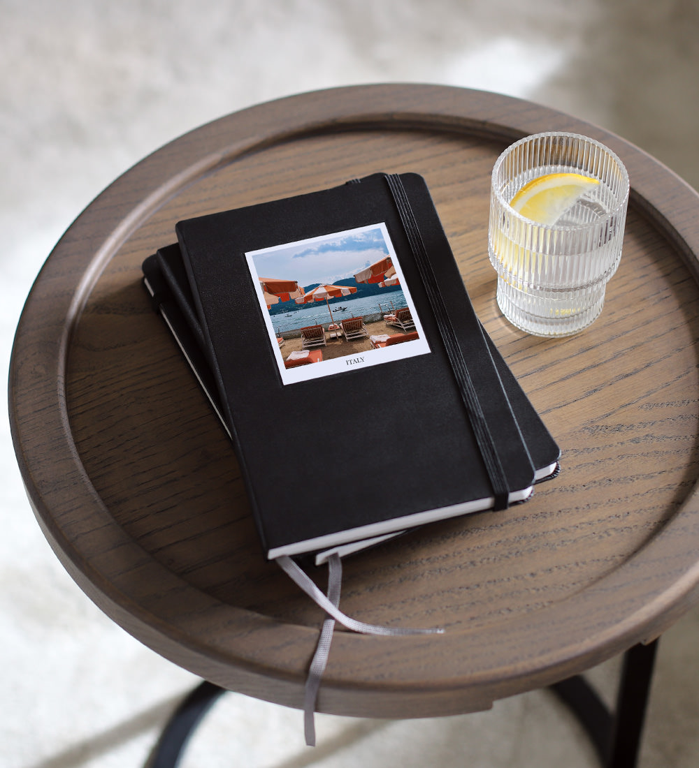 Portrait Moleskine Photo Books stacked on wooden stool table with Italy photo on cover.