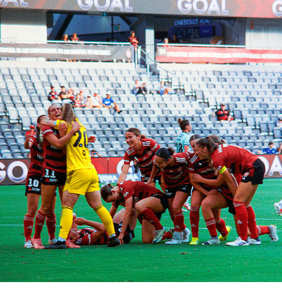 Women's rugby team smiling together on field in red uniforms.