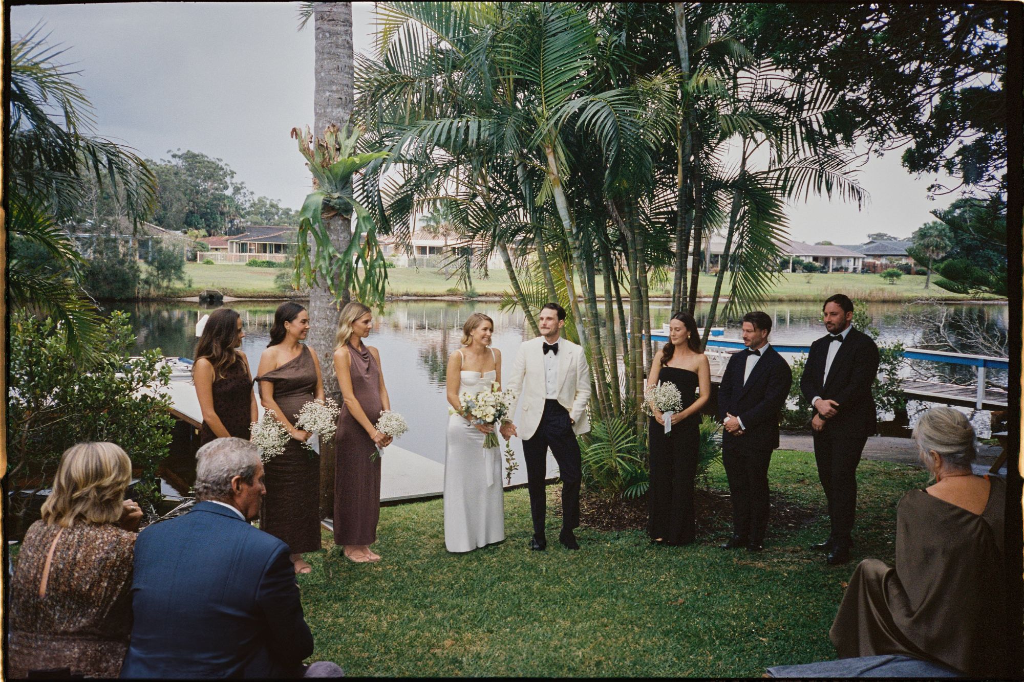 Couple standing amongst their wedding party under palm tree