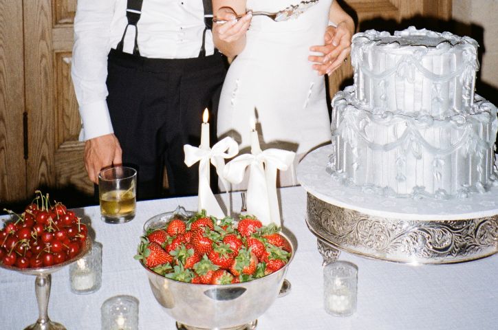 Couple from the neck down with white wedding cake and strawberries