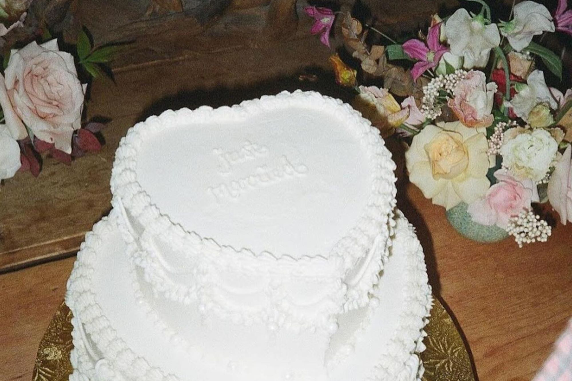 White vintage piped icing cake surrounded by delicate pastel wedding flowers.