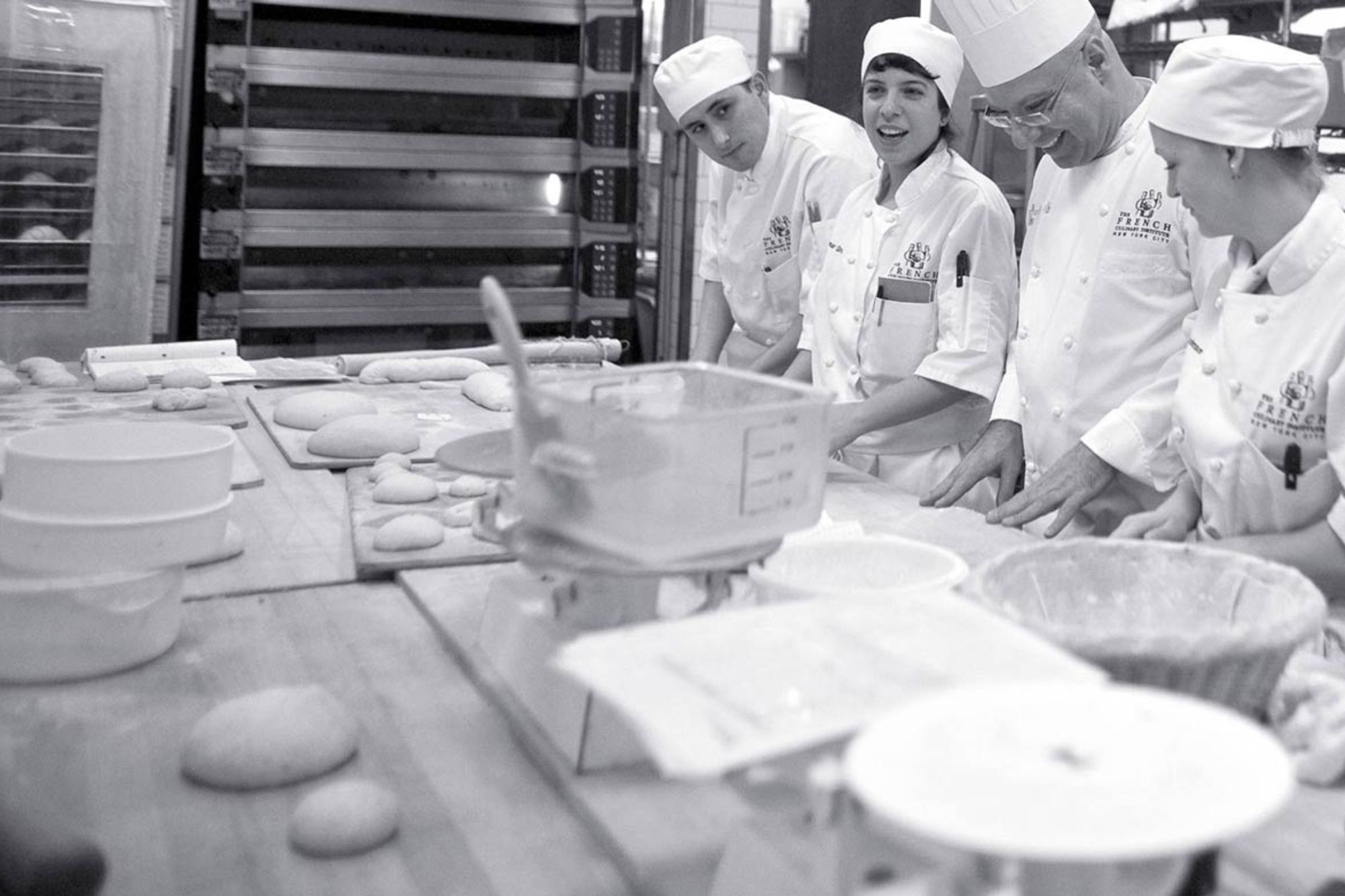 Bakers in kitchen smiling together in front of balls of dough.