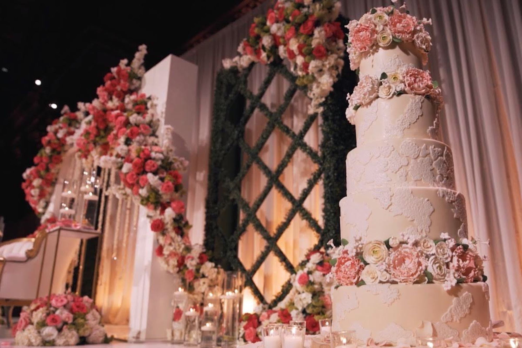 Lace covered five-tiered wedding cake covered in pink and white sugar flowers.