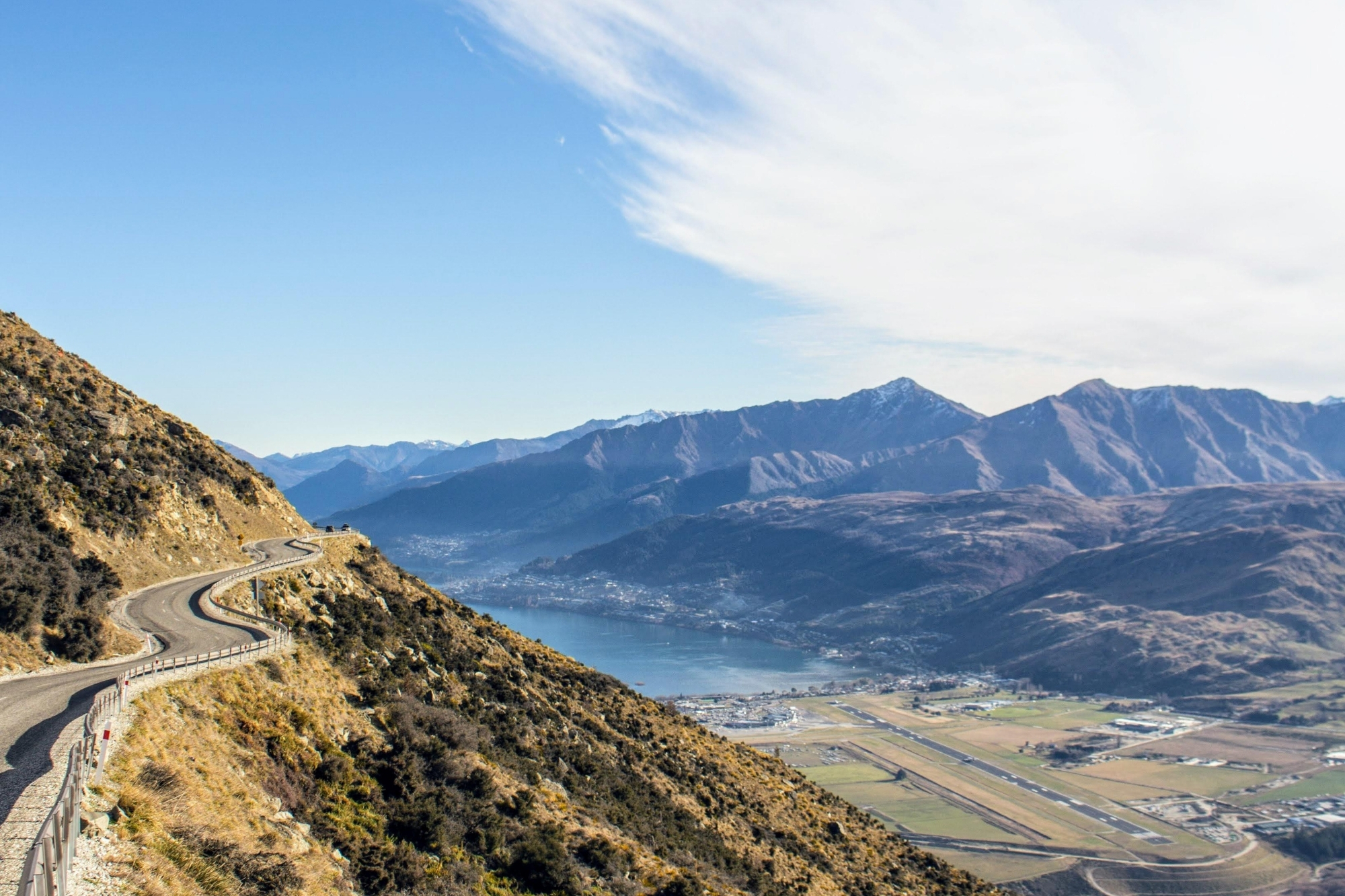 Mountainside road overlooking Queenstown and distant mountains.