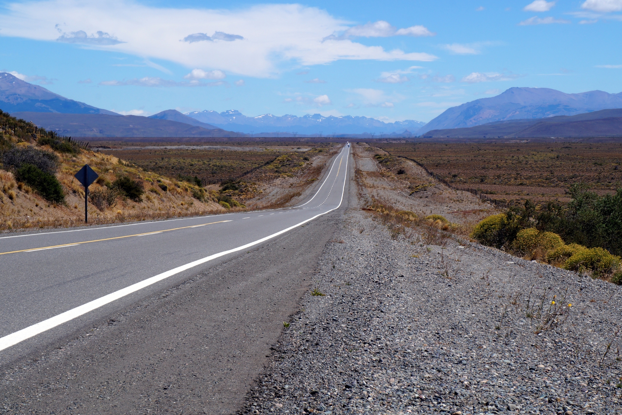 Open straight road on flat land heading towards mountainous landscape in Argentina.