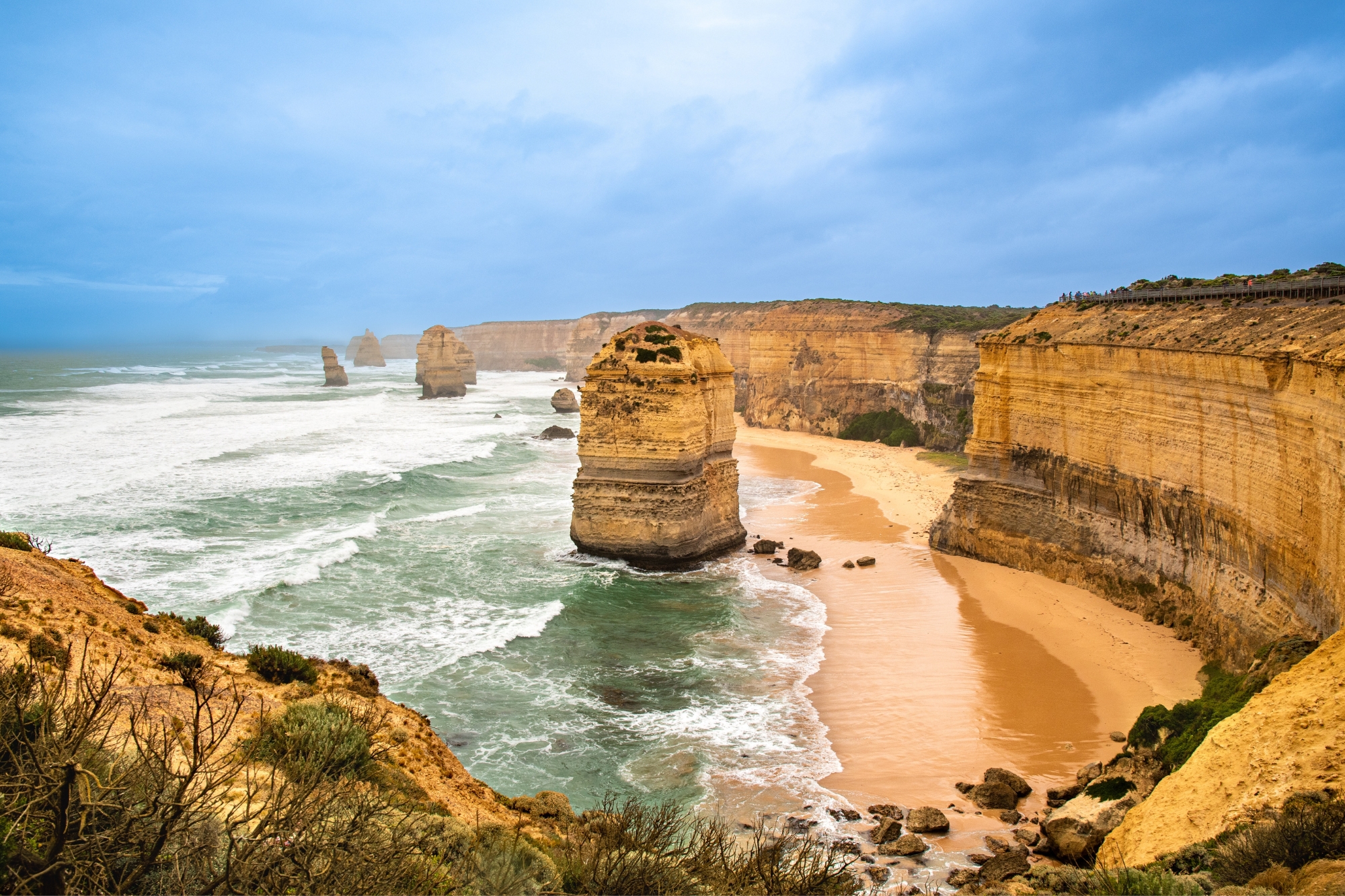 Orange hued cliff faces with white capped crashing shore in Australia.