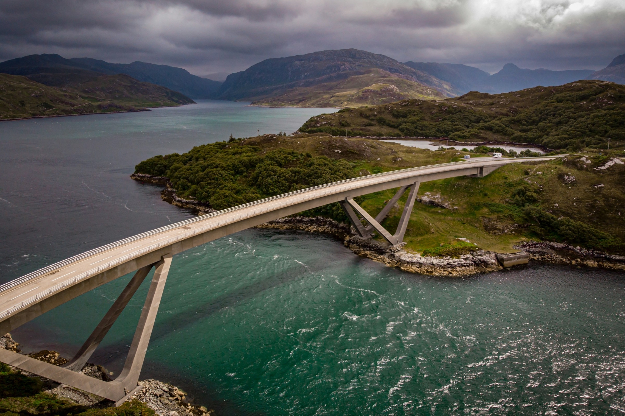 Long bridge road in Scotland connecting two patches of land underneath a stormy sky.