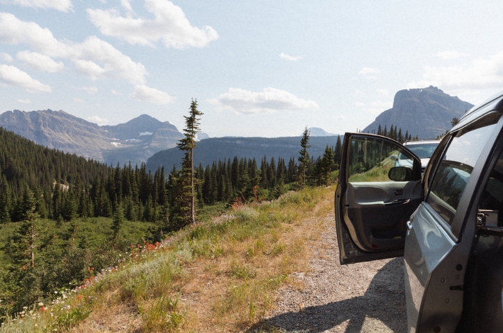 Car driving along road overlooking forest on sunny day.