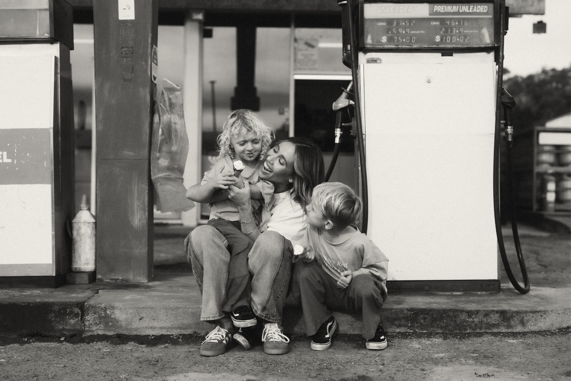 Black and white photo of mother and children sitting at edge of gas refillery with ice creams.