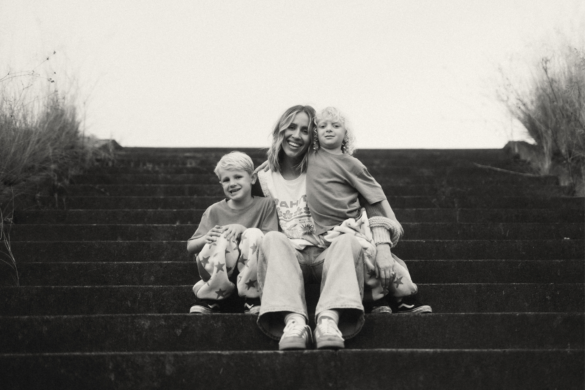 Mother and her two suns sit together on steps smiling.
