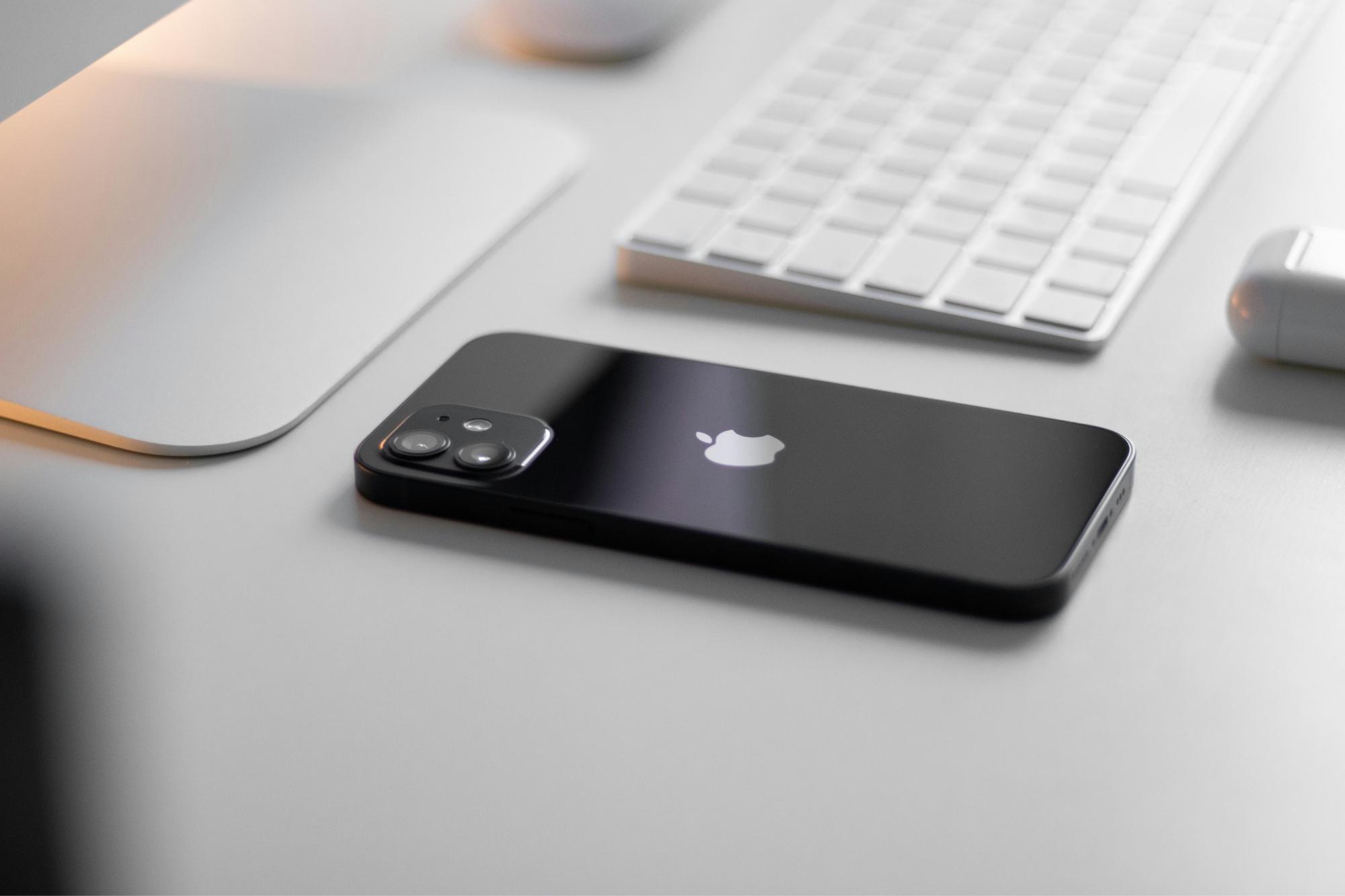 Black iPhone 7 laying on white desk face down next to white Mac keyboard.