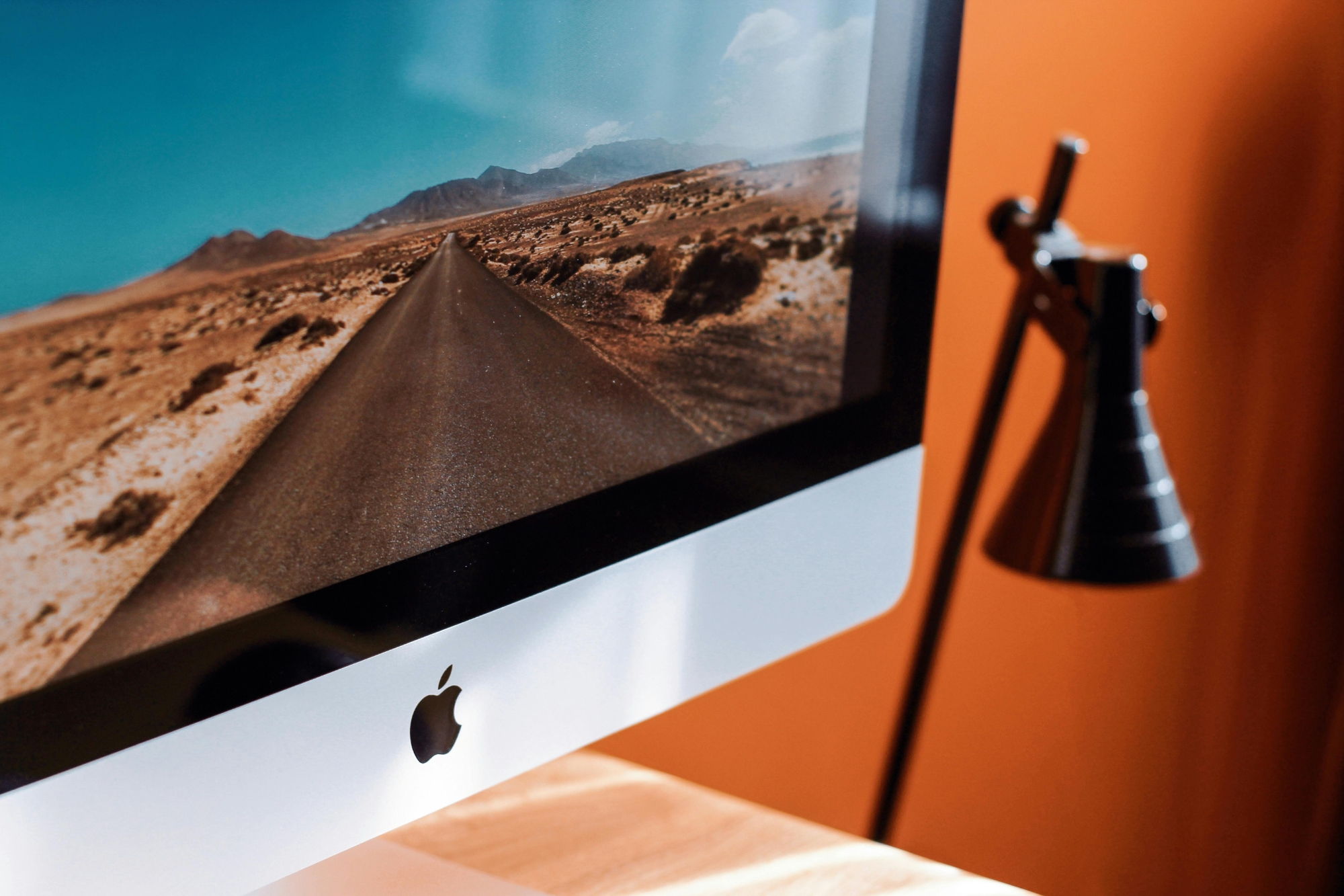 Close up of Mac desktop screen and table light against orange wallpaper.