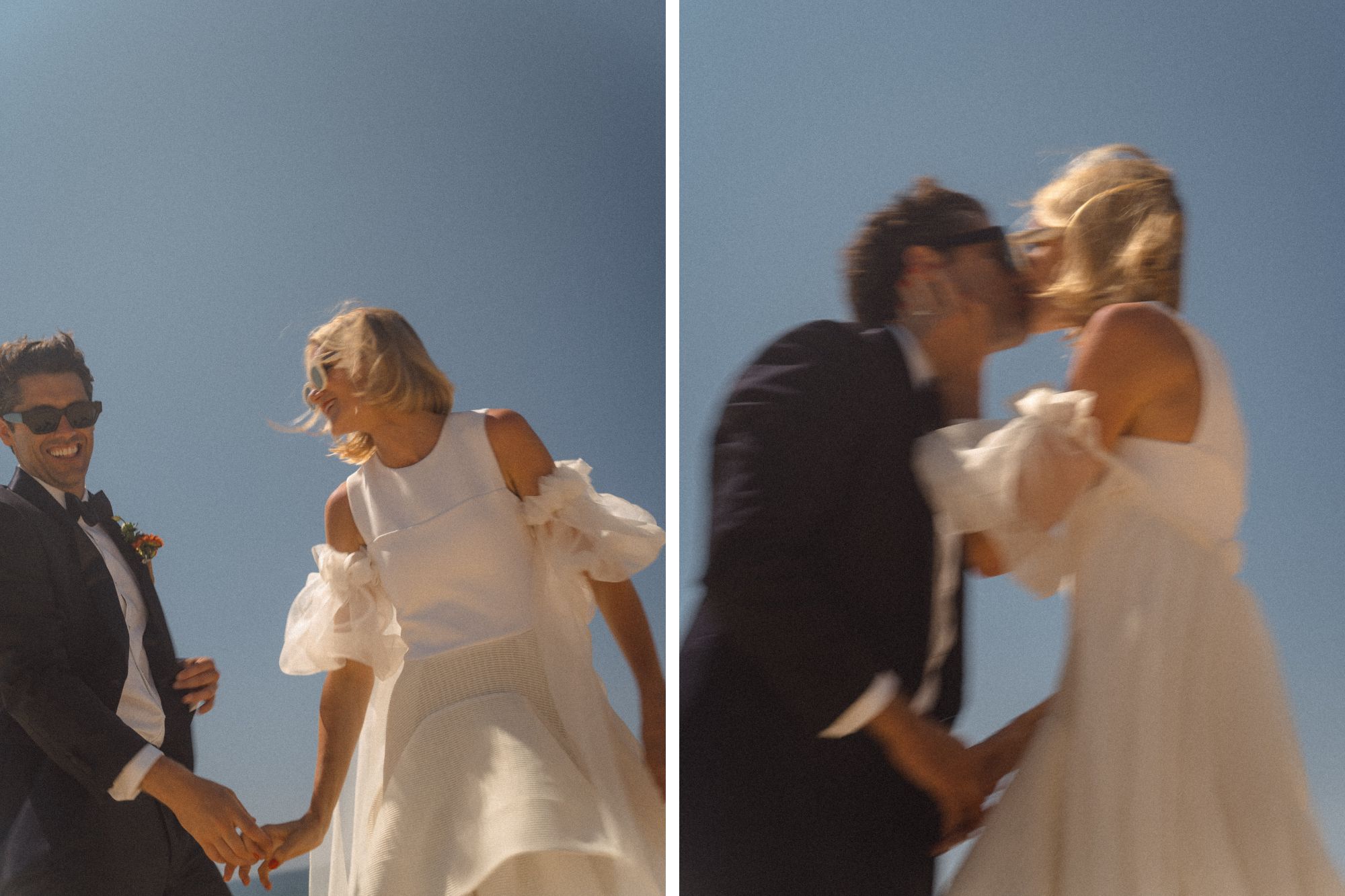 A happy newlywed couple wearing sunglasses hold hands and kiss under bright sunlight and blue sky.