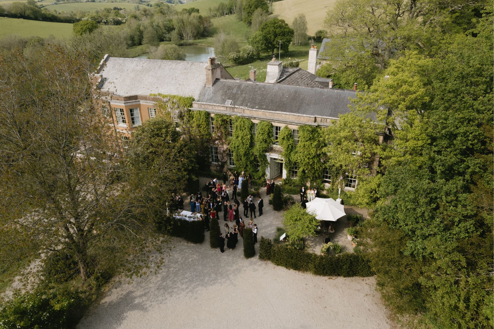 Wide shot of wedding guests in black tie attire standing outside historical mansion venue at wedding reception.