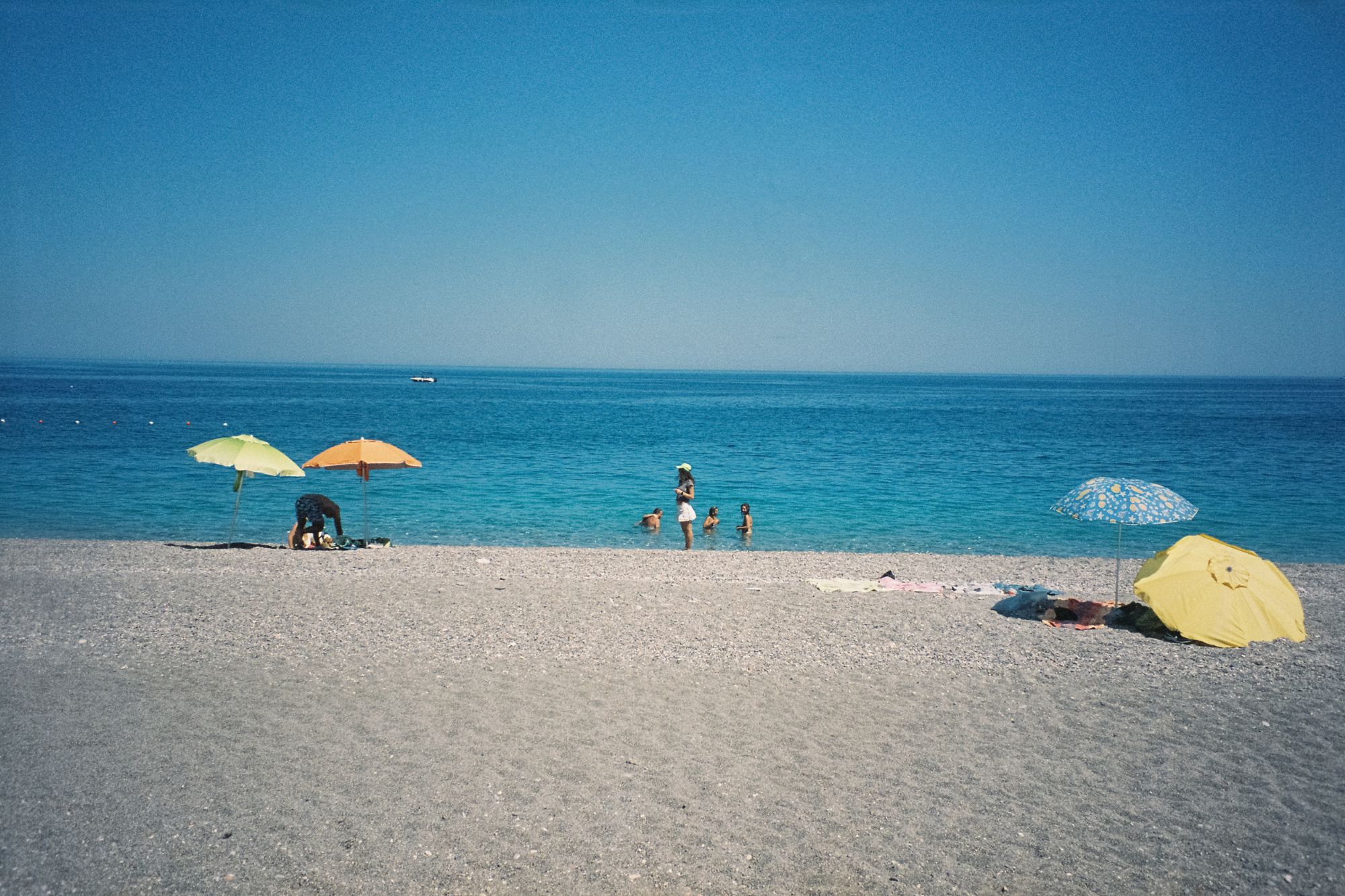 People under umbrellas enjoying shelly beach and flat, calm ocean water.