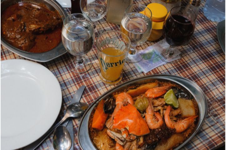 Picnic blanket with food laid out with wine glasses in center of blanket.