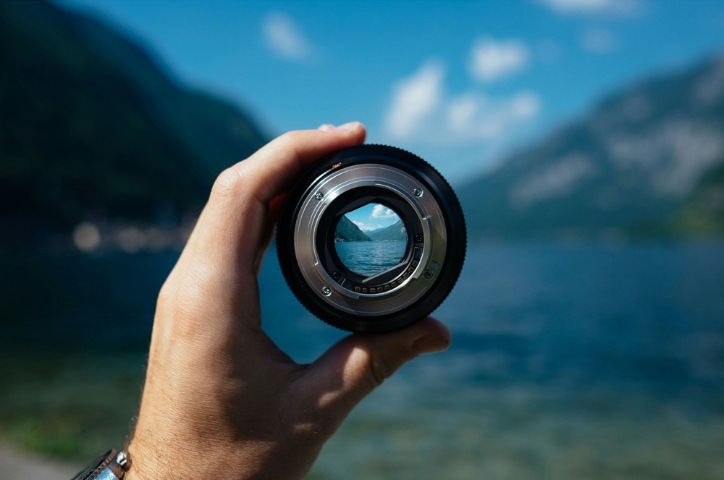 Hand with a circle lens focusing on a spot in lake under bright blue sky.