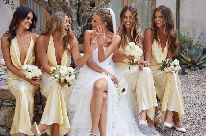 Bride sitting next to bridesmaids in pastel yellow dresses with matching mini bouquets.