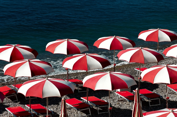 Bright red and white umbrellas line shoreline on Italian beach with no people underneath.