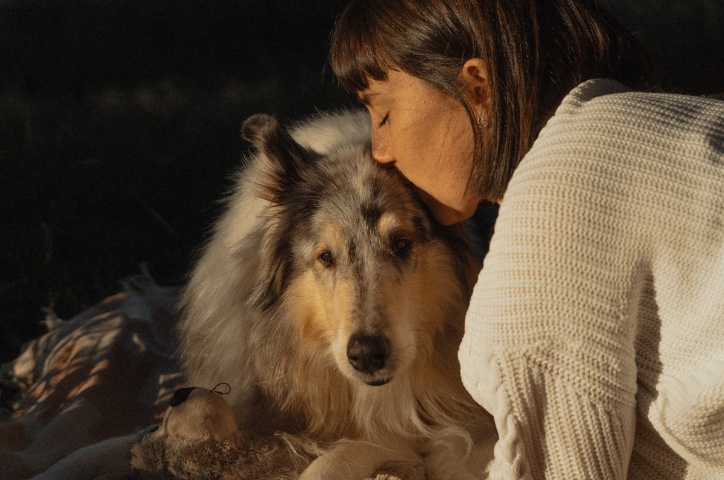 Woman kissing Australian shepherd dog's head.
