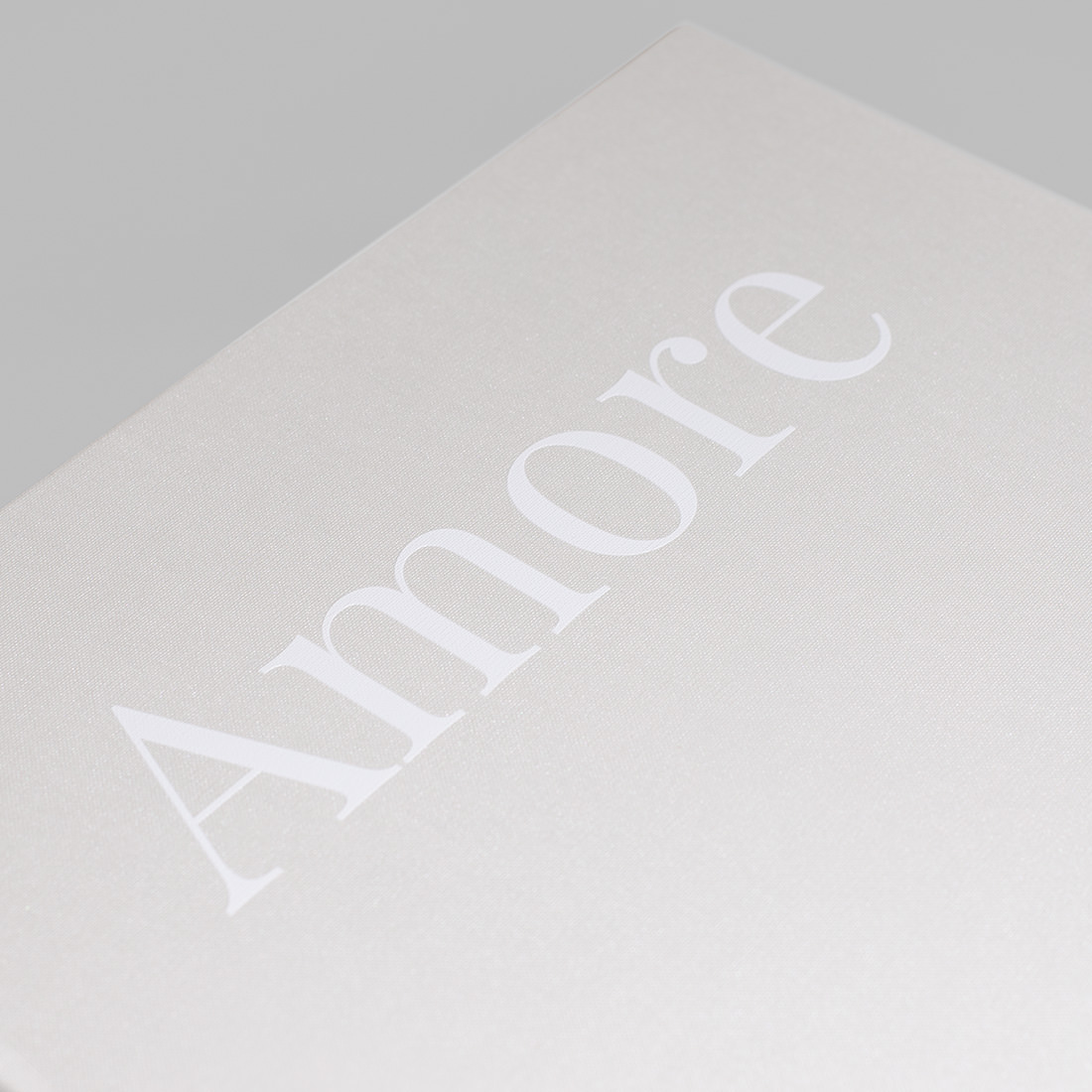Close up of white coated cloth cover with white UV printed text reading 'Amore'.