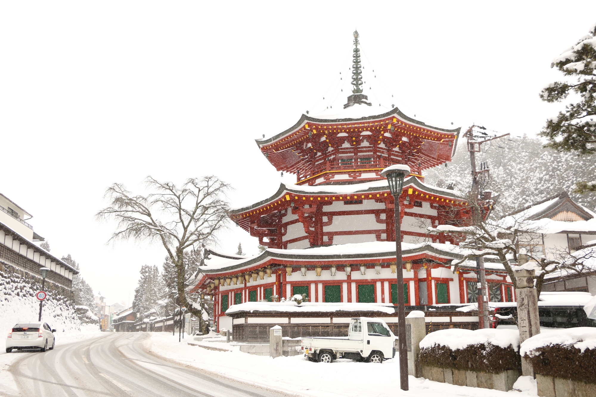 A Japanese temple covered in snow with a small truck parked beside it on the road.