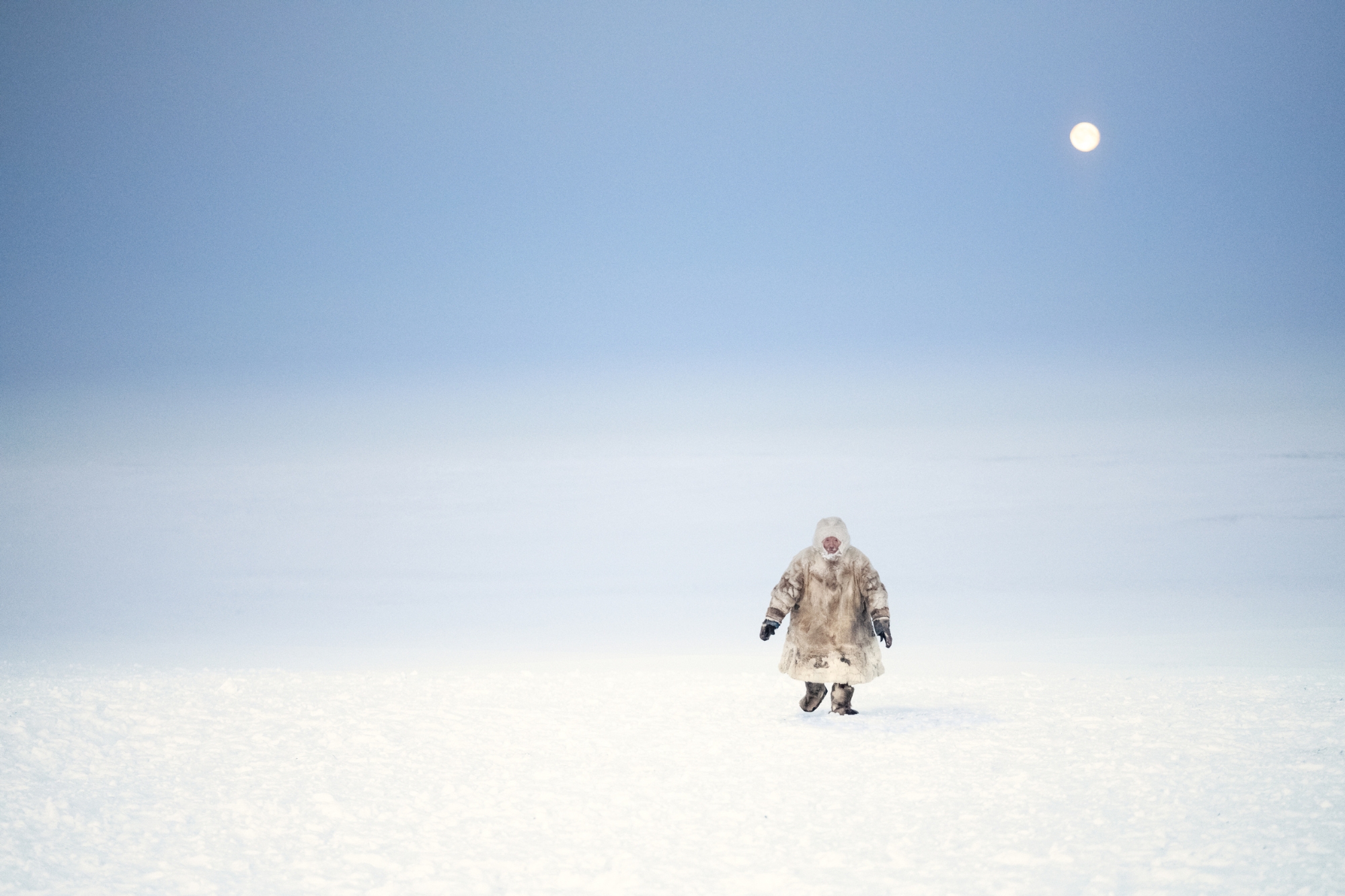 Man in fur one piece poncho strides through thick snow in Antarctica.