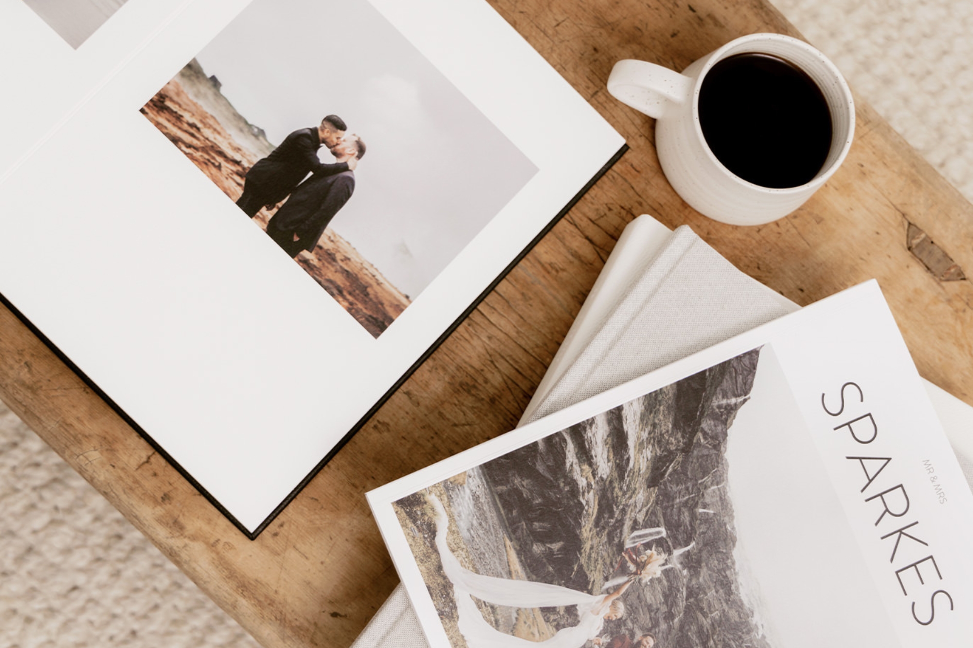 Wedded couple kiss in black suits on rocky flat land, inside a black portrait photo book.