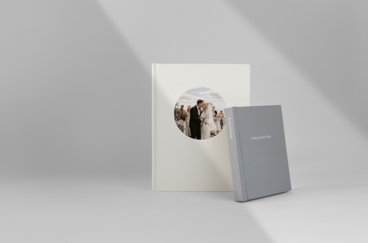 Two Portrait Premium Photo Books standing leaning on each other on grey background.
