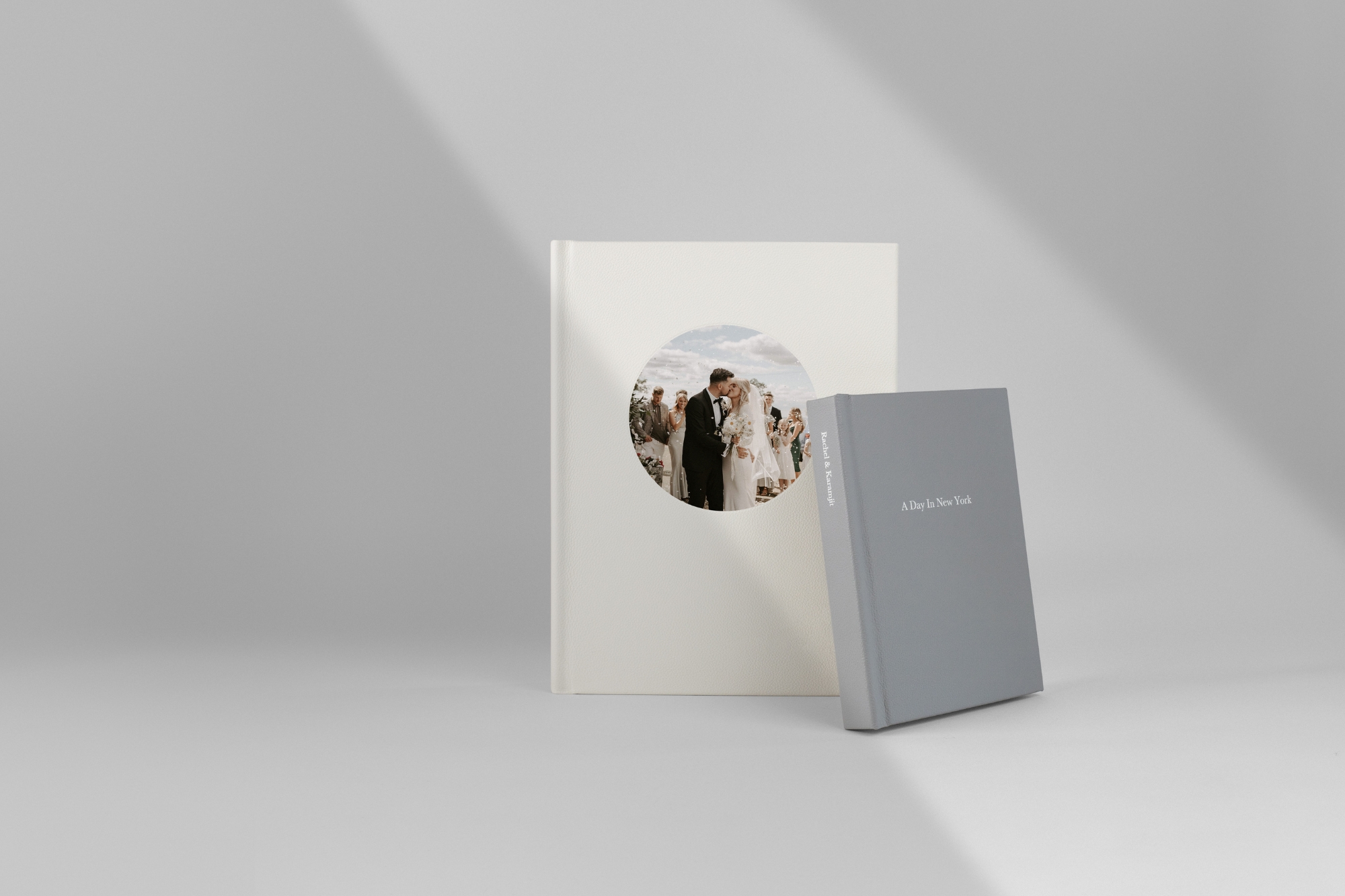 Two Portrait Premium Photo Books standing leaning on each other on grey background.