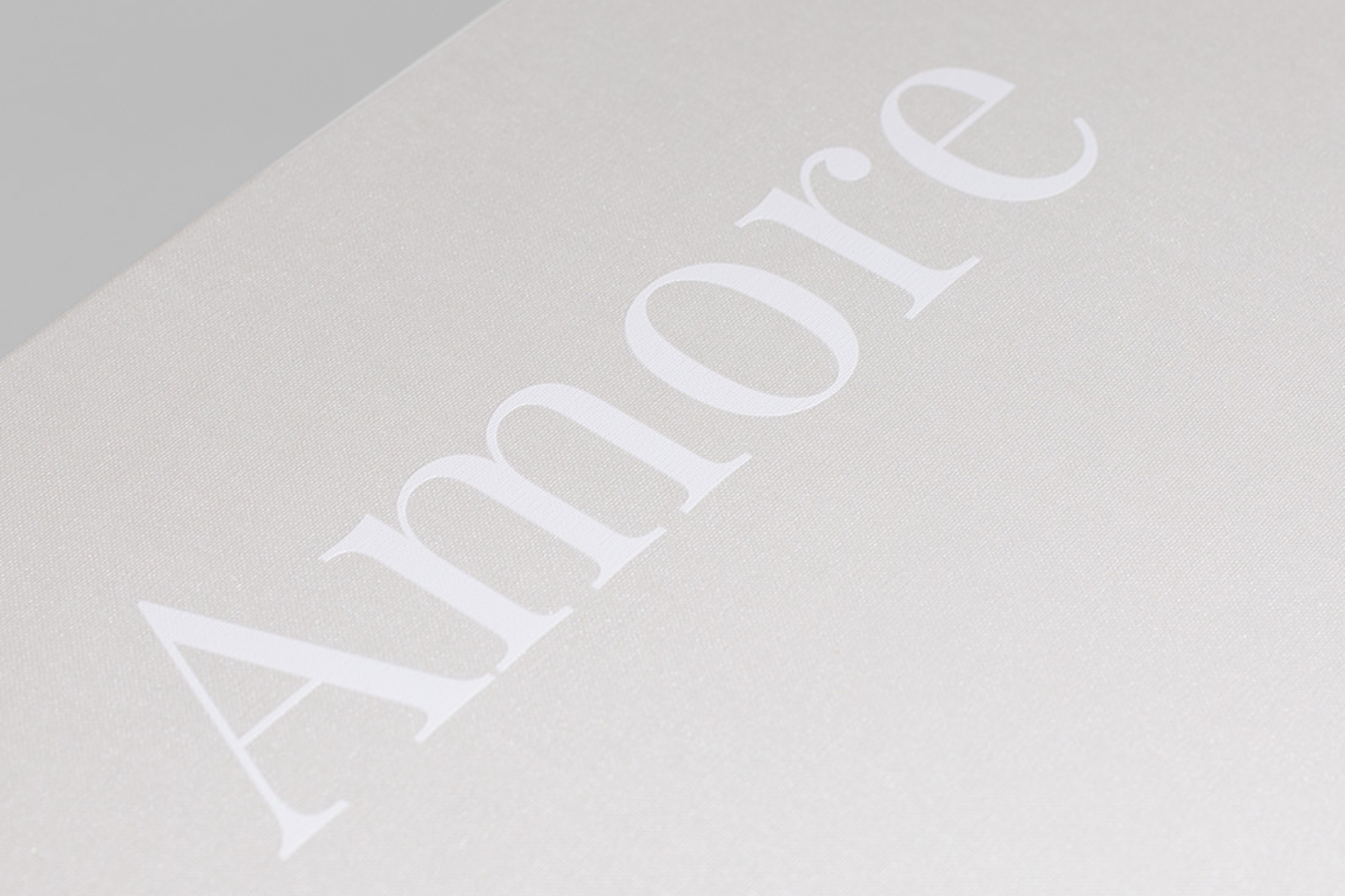 Close up of UV printed text on cover reading "Amore" in white ink, on natural ivory premium linen cover fabric.