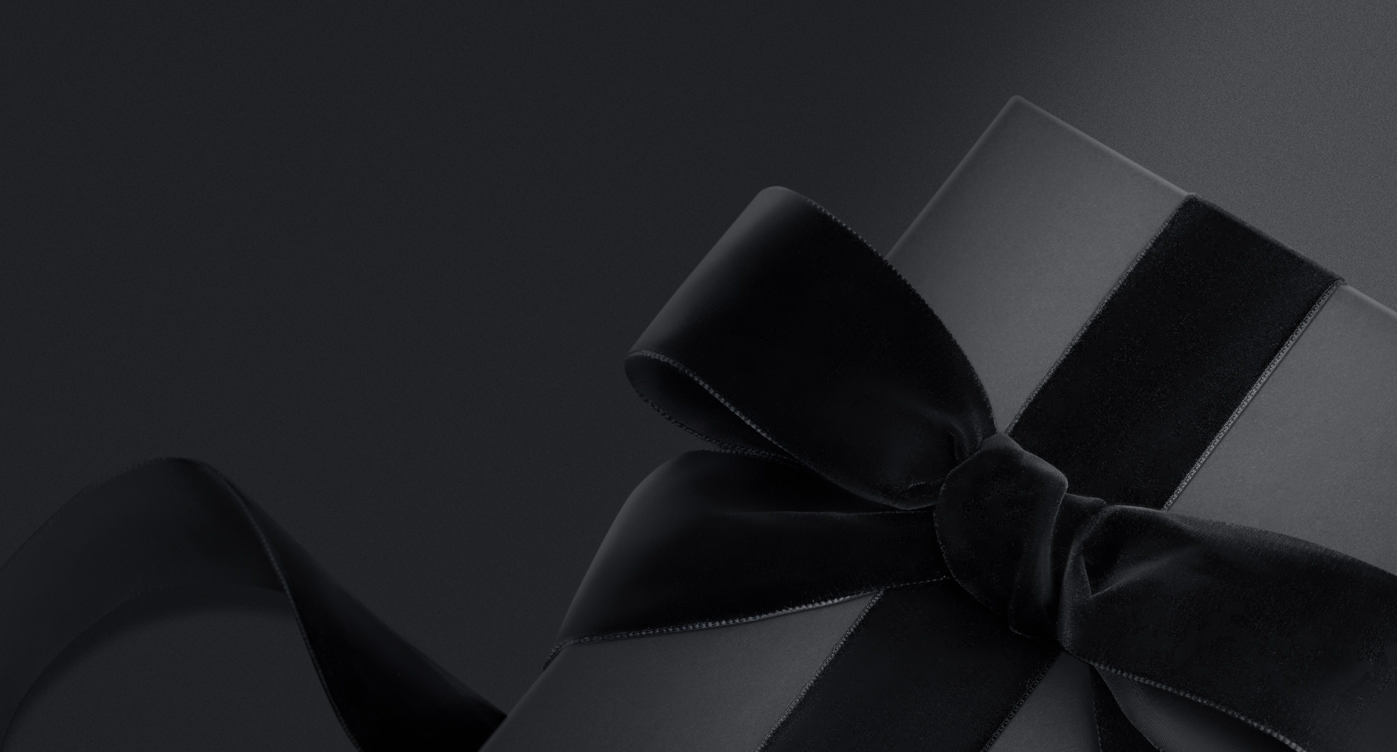 Boîte cadeau noire avec un ruban noir en velours sur un fond noir sombre.