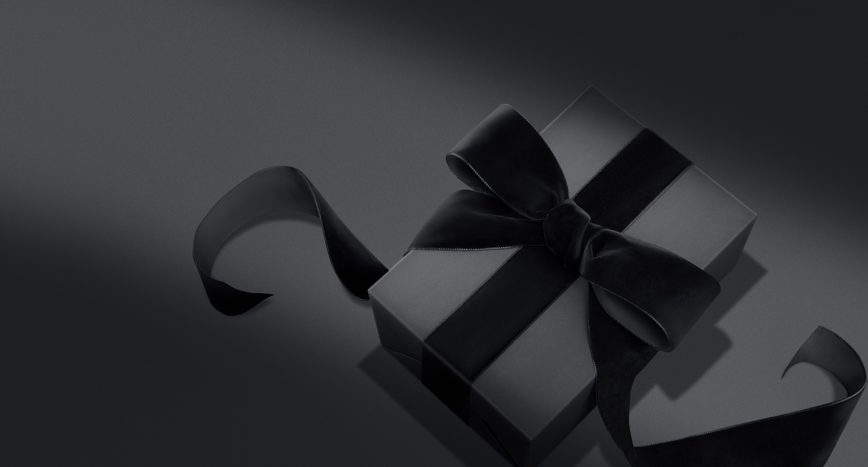 Black gift box wrapped with a velvet black ribbon on shadowy black background.