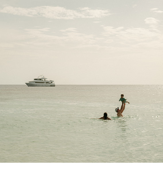 Couple lifting a toddler while swimming in ocean under late midday sunshine.