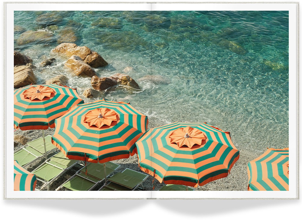 Open Portrait Premium Photo Book showing bright beach with clear turquoise water and matching green and orange umbrellas on the shore.