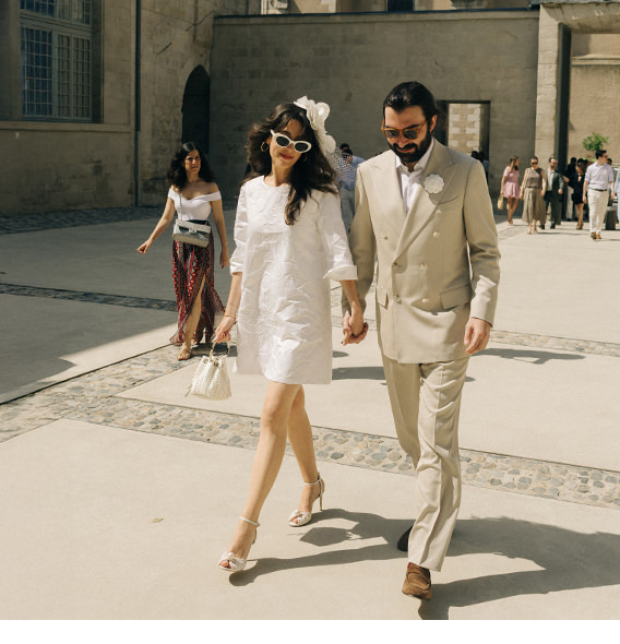 Newlywed couple walking hand in hand across courtyard.
