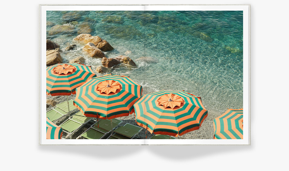 Open Portrait Premium Photo Book showing bright beach with clear turquoise water and matching green and orange umbrellas on the shore.