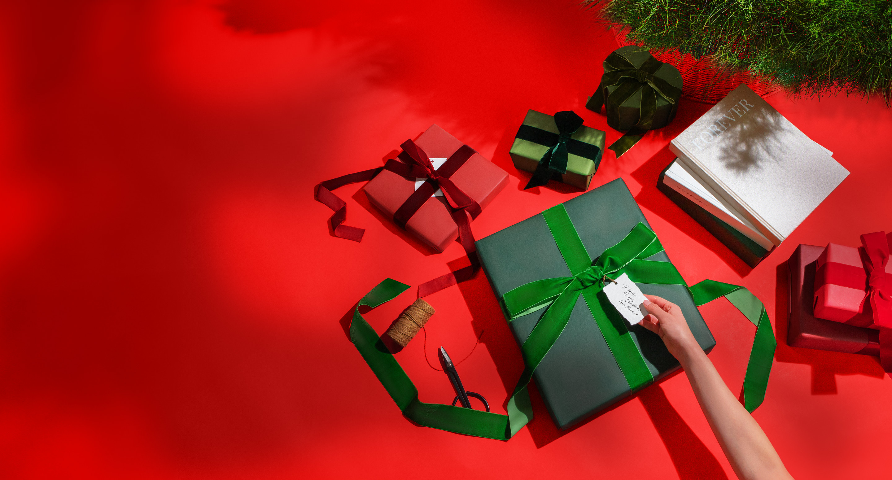 Tying red ribbon on Christmas wreath laying on bright red background.