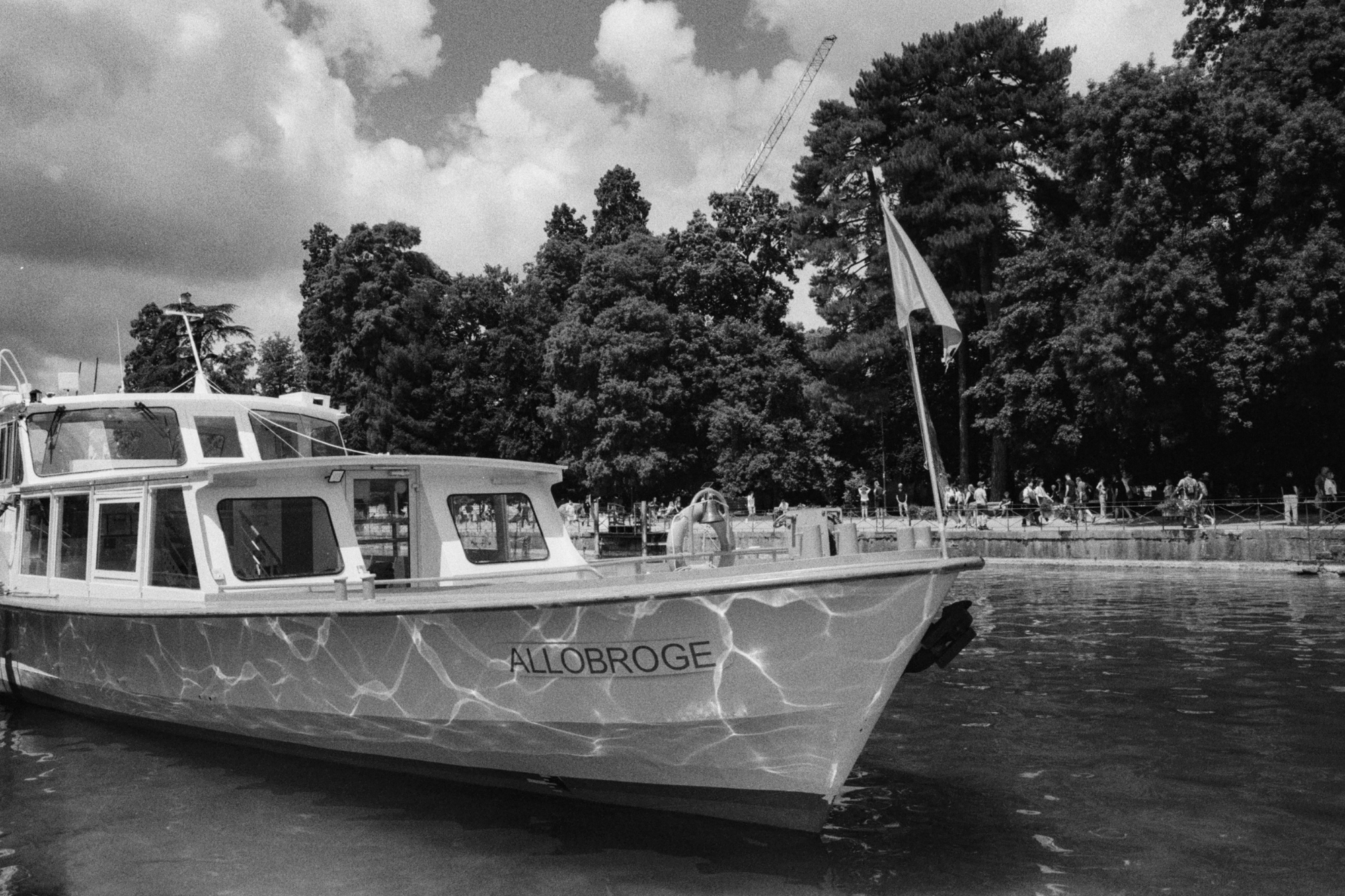 Boat named 'Allobroge' with water reflections on hull, lined next to walking path in park.