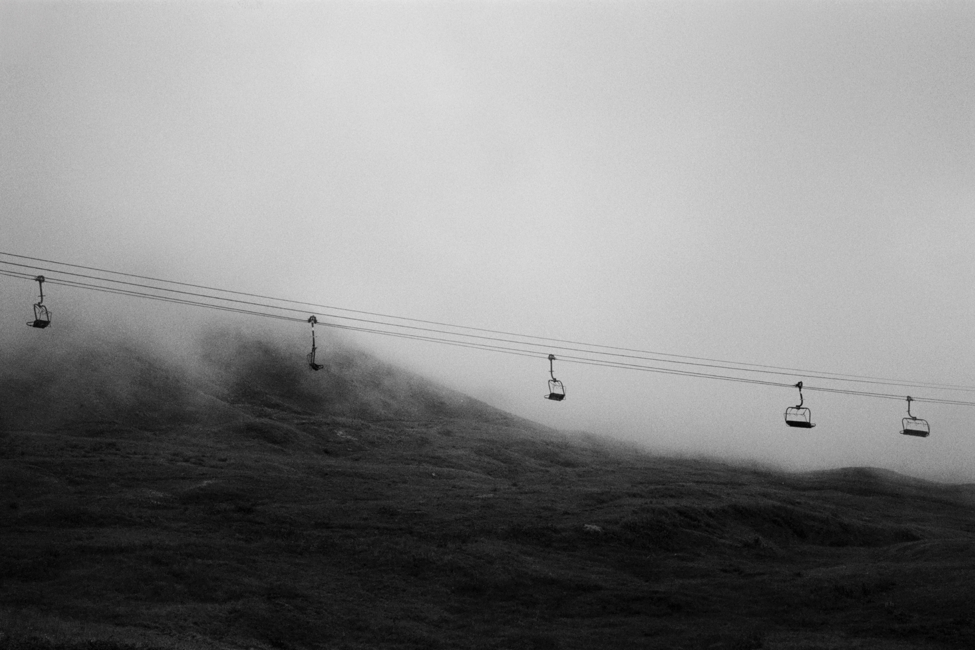 Line of gondolas moving over a misty hill.