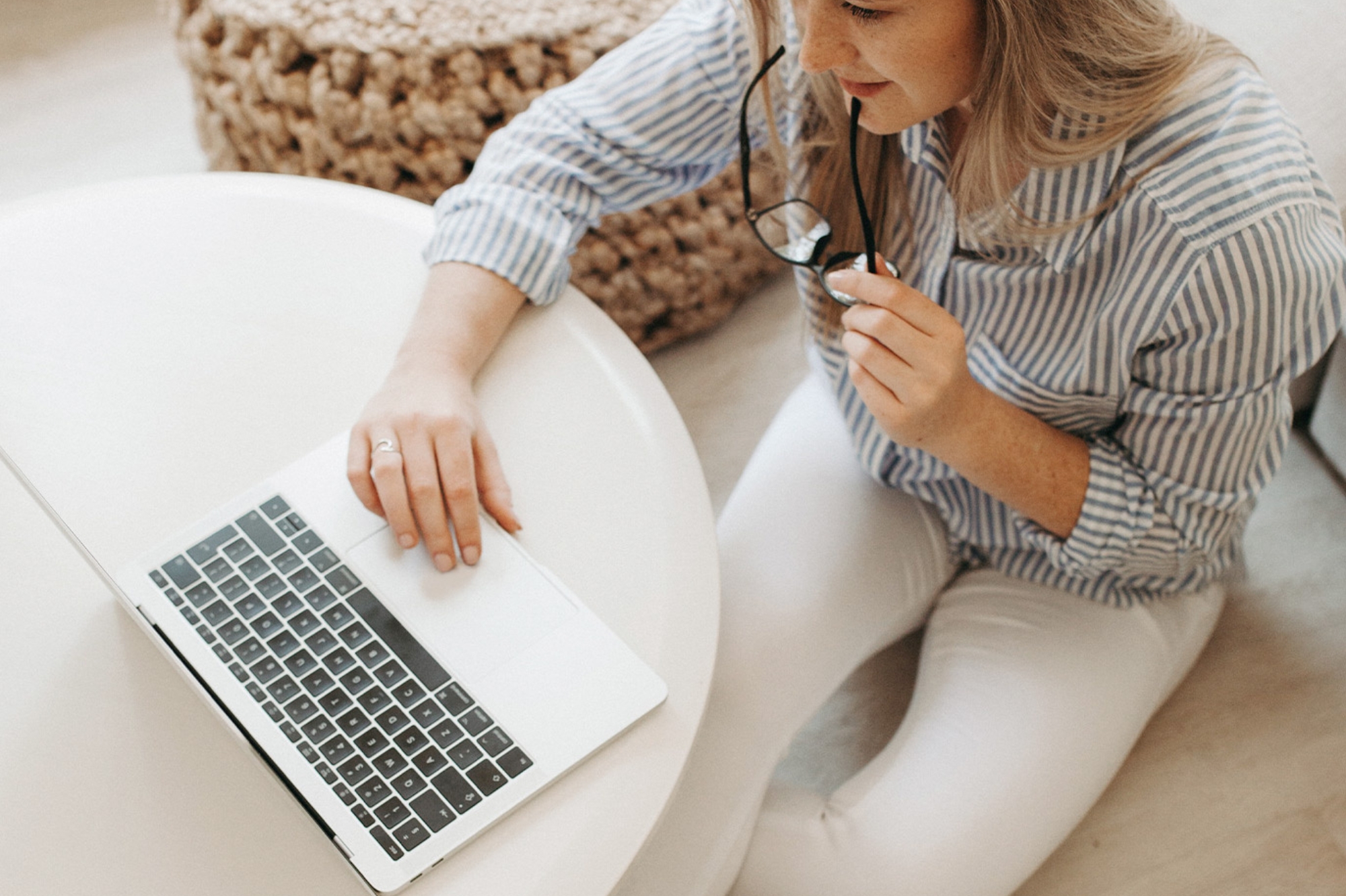 Woman browsing on laptop while fiddling with black reading glasses.