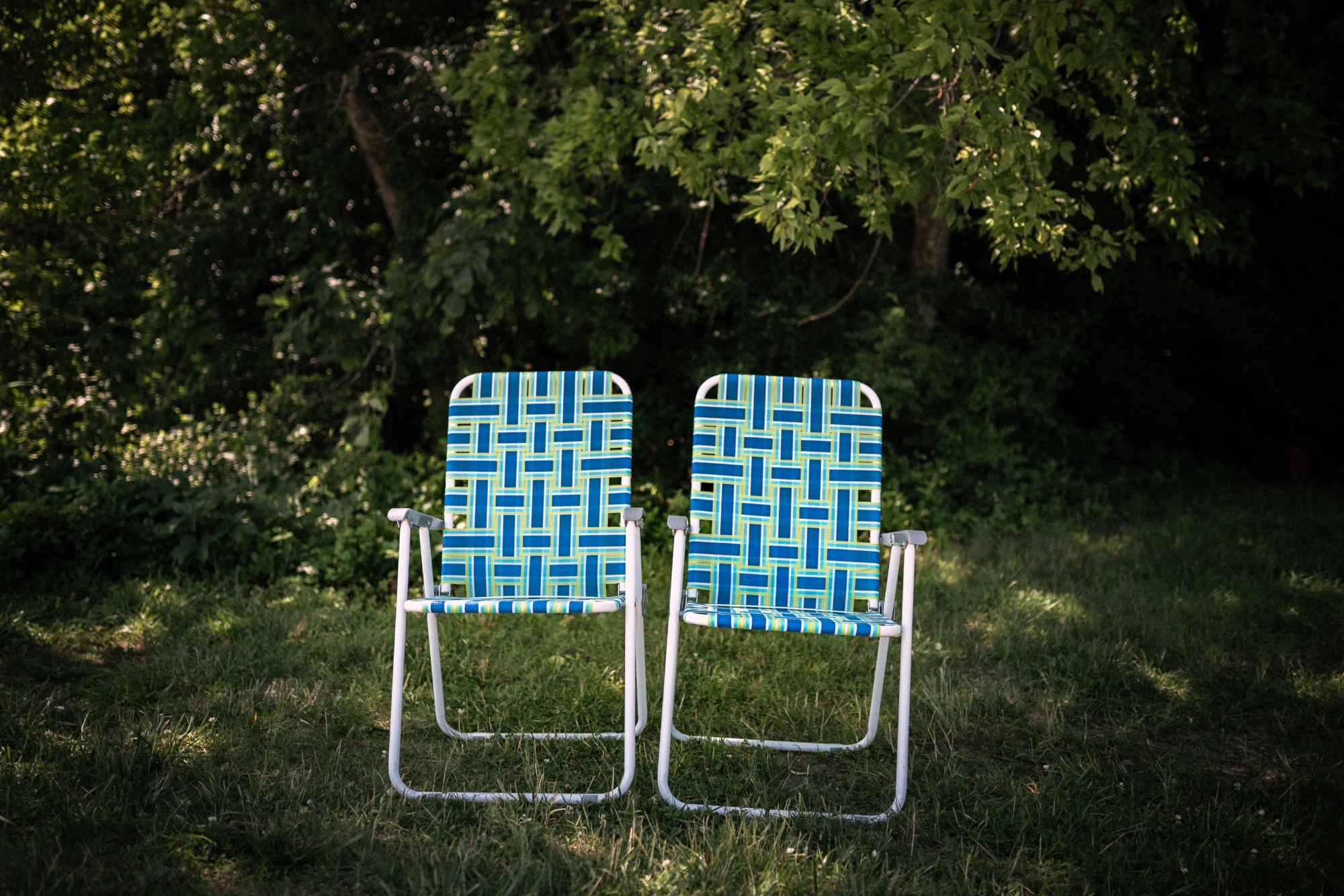 Two blue chairs sitting in front of lush green trees and shrubs.
