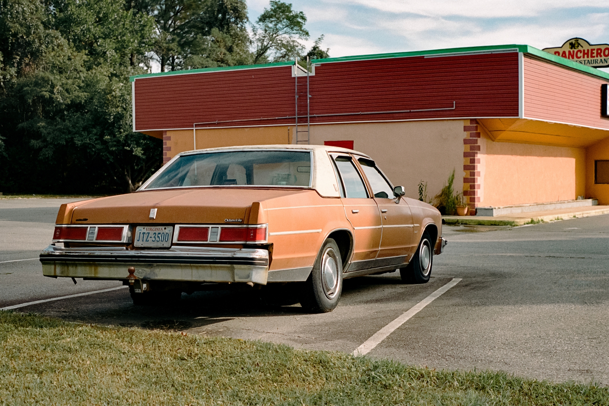 Vintage orange Oldsmobile parked outside an old retro fast food restaurant.