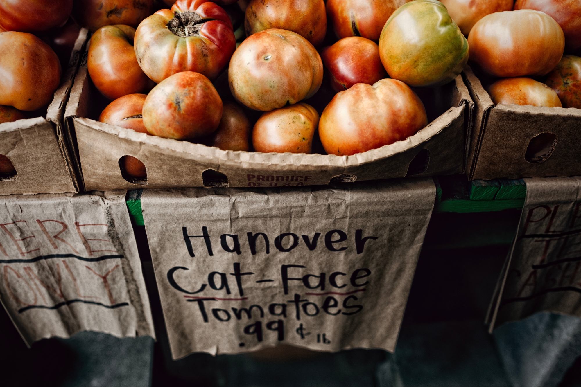 Stacks of tomatoes in cardboard baskets with handwritten paper signs with prices listed.