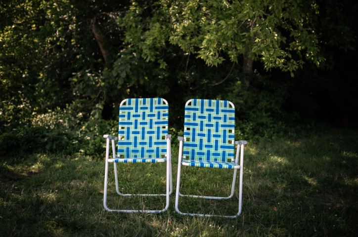 Two blue chairs sitting in front of lush green trees and shrubs.