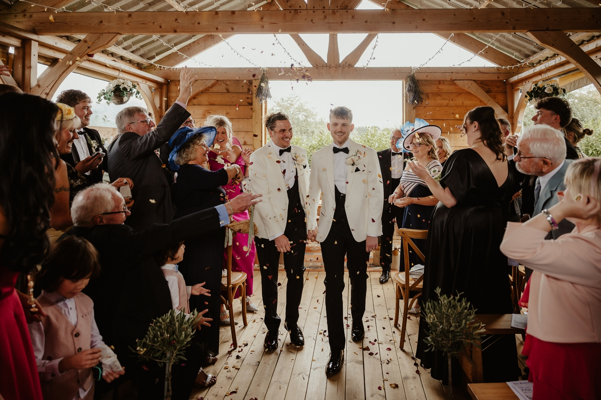 The two grooms walking down the aisle with flower petal confetti thrown at them.