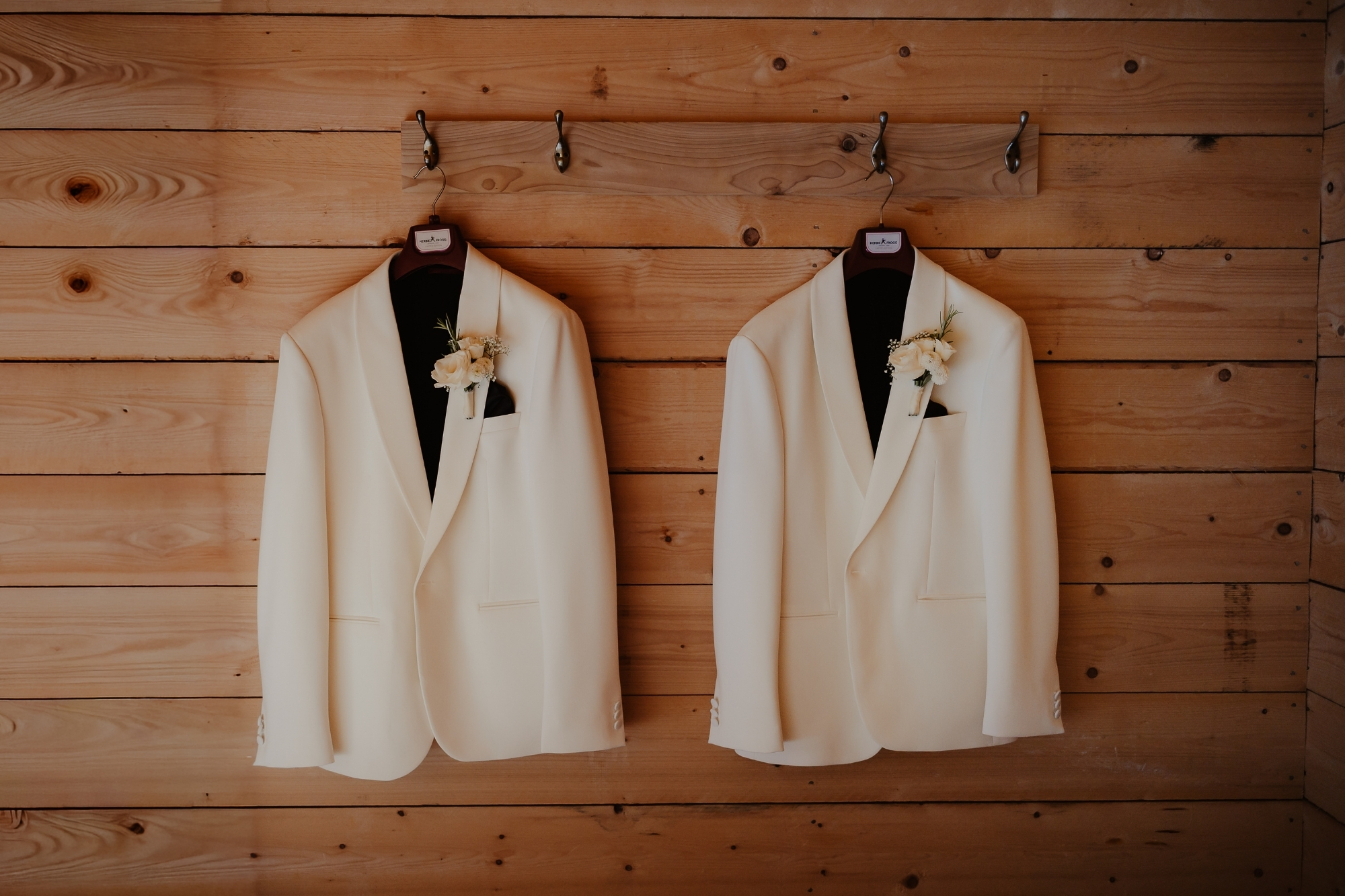 Two white blazers hanging on wooden wall.