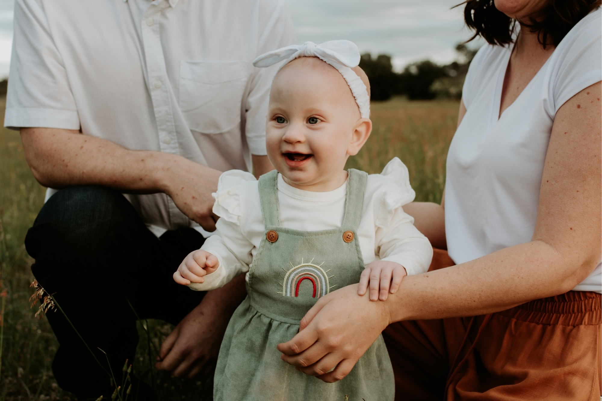 Infant girl smiling while being held by parents.