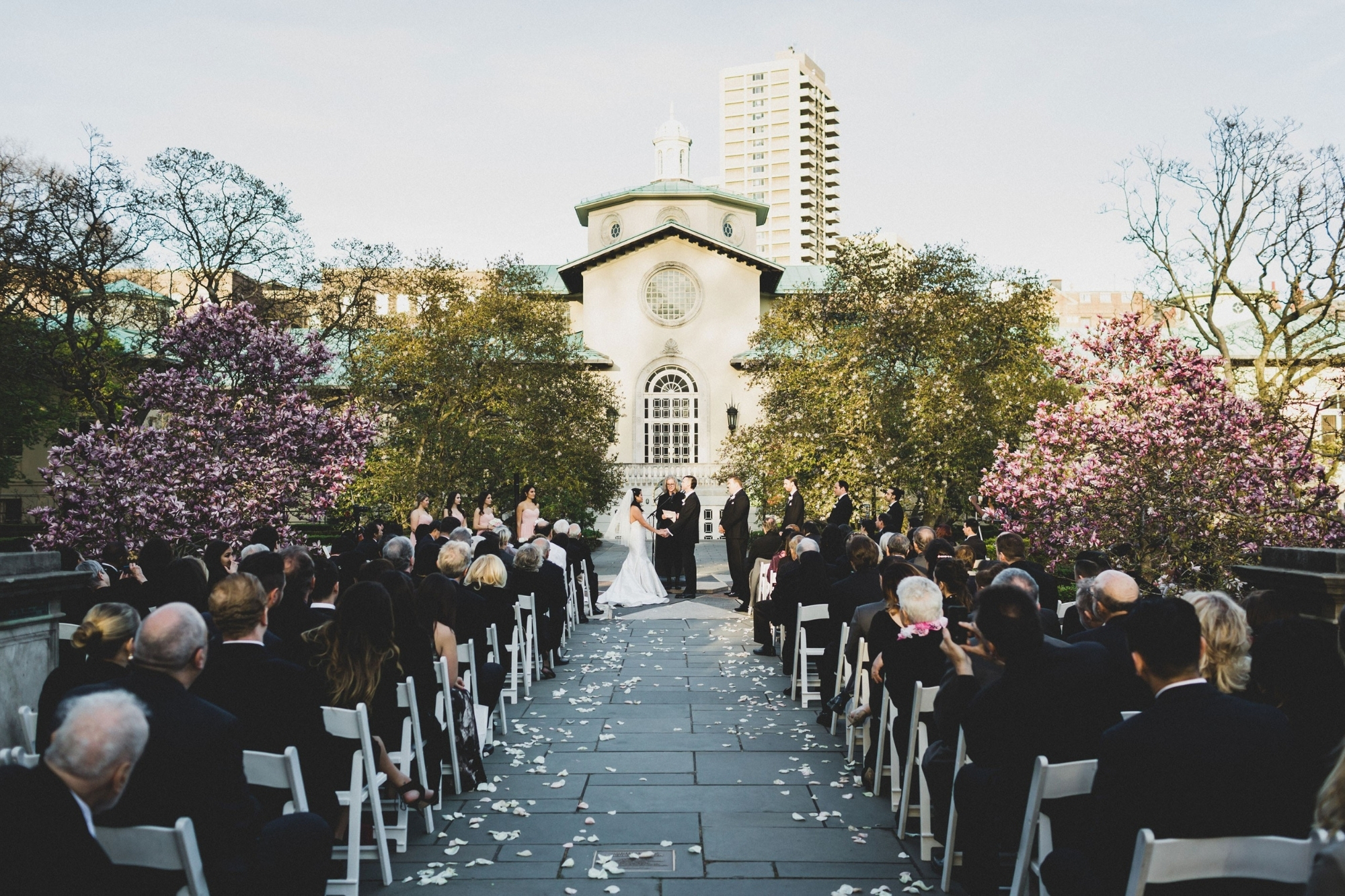 Bride and groom look at each other at end of petal covered wedding aisle at the Brooklyn Botanic Garden.