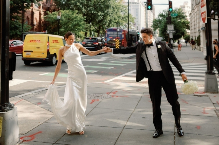 Bride and groom hold hands with arms stretched while walking through streets of Brooklyn.